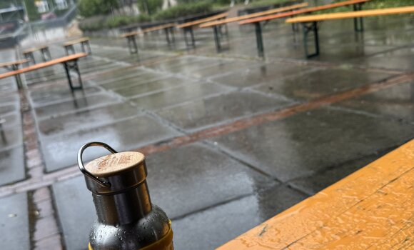 Zu sehen ist eine Trinkflasche des LHR auf einer Bierzeltgarnitur im Regen. 