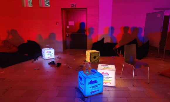 Zu sehen ist die Partylocation mit den LHR LED-Sitzwürfeln, die im dunkeln in bunten Farben leuchten. Außerdem kann man an der Wand Schatten von den tanzenden Partygästen sehen. 