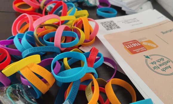 Auf dem Bild ist ein Tisch mit Werbematerial von "Nummer gegen Kummer", dem Landesheimrat Bayern, dem Projekt "Mits eine Frist" des Bundesnetzwerk Ombudsstellen zu sehen. Auf dem Tisch liegen Armbänder, Flyer und Sticker.