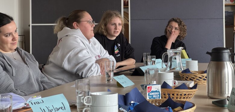 Zu sehen sind die LHR Vertreterinnen, die an dem Arbeitsgespräch teilgenommen haben. Sie sitzen an einem Tisch, der mit Kaffee und Wasser gedeckt ist und beteiligen sich an der Diskussion.